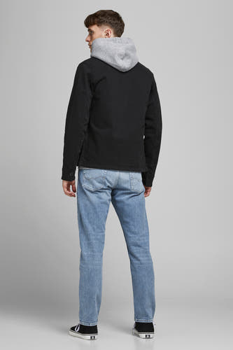 Jean slim en denim de JACK & JONES JEANS INTELLIGENCE, avec un lavage bleu clair, porté avec une veste noire et des baskets.