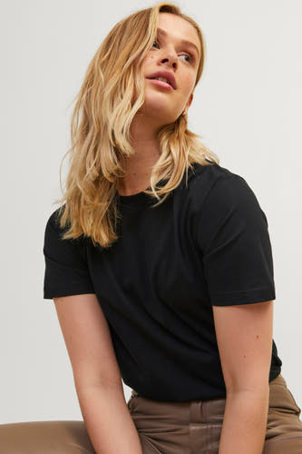 T-shirt noir de JJXX, porté avec un pantalon en cuir marron et des cheveux blonds détachés.