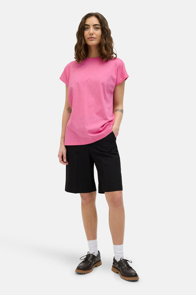 T-shirt rose à manches courtes de JJXX, porté avec des shorts noirs, des chaussettes blanches et des baskets brunes.