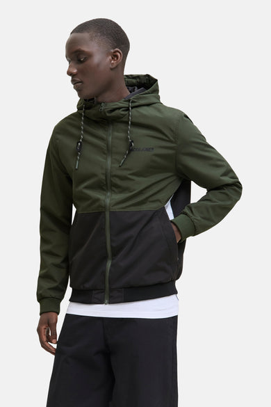 Veste de pluie verte d'ORIGINALS BY JACK & JONES, avec des blocs de couleur noirs et un capuchon, portée sur un T-shirt blanc et une pantalon noir.