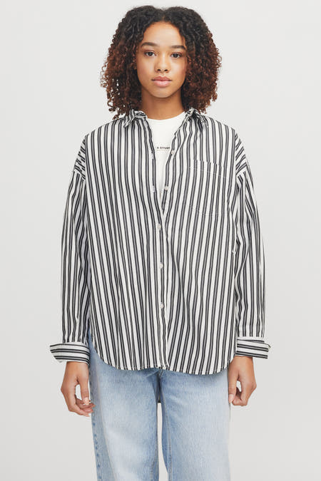 Chemise rayée blanche et bleue à manches longues de JJXX, portée sur un T-shirt blanc et des jeans denim légers.