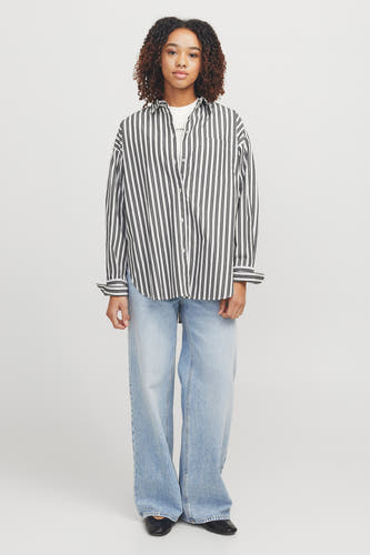 Chemise blanche à longues manches de JJXX, avec des rayures noires verticales, portée avec un pantalon en cuir.
