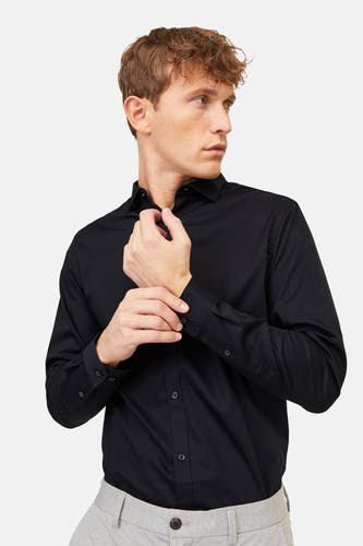 Chemise noire à manches longues de PREMIUM by JACK & JONES, gros plan sur un homme boutonnant sa manche, avec un pantalon gris.