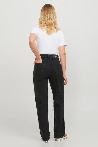 Vrouw met blond haar, witte top, zwarte jeans, en Converse schoenen, achterkant.