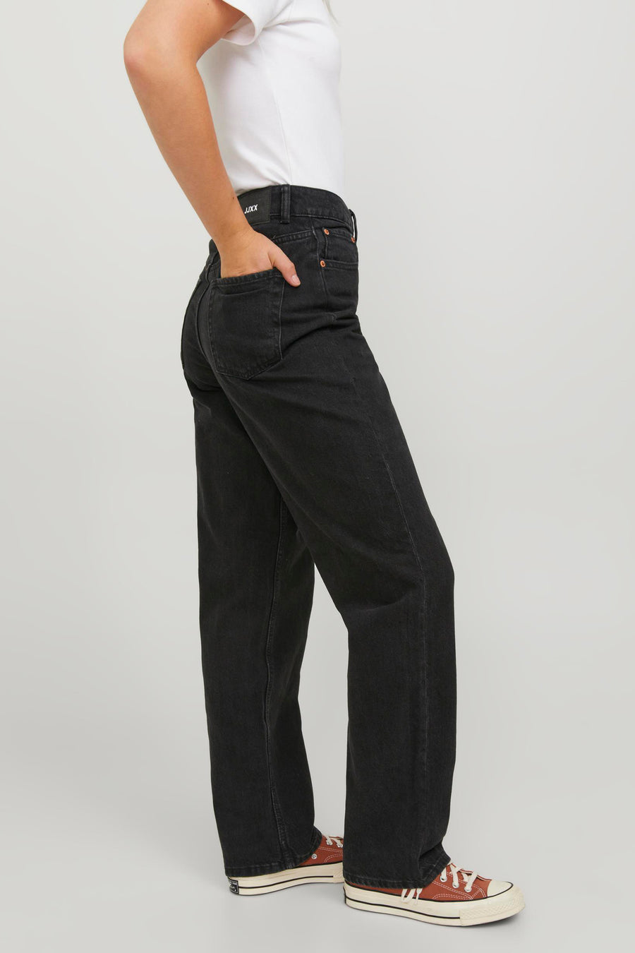 Persoon in zwarte jeans en rode Converse sneakers.