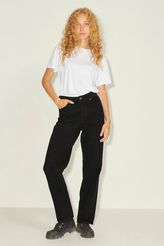 Model met blond krullend haar, witte t-shirt, zwarte jeans en zwarte boots, poseert voor een witte achtergrond.