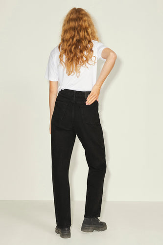 Vrouw met rood haar, witte T-shirt, zwarte jeans, zwarte schoenen, staand.
