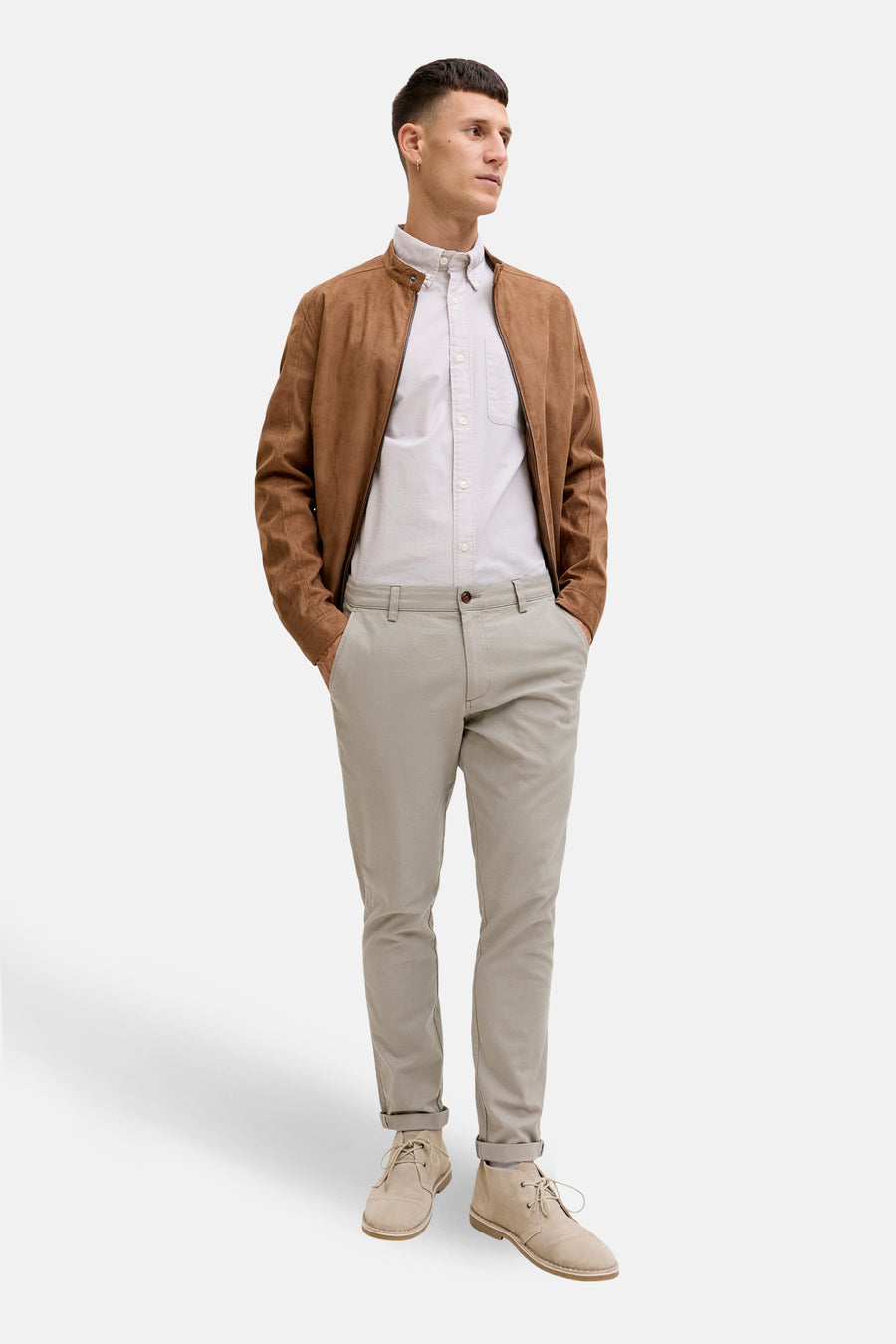 Man in bruin suède jack, lichtgrijs overhemd, beige chino en suède schoenen.