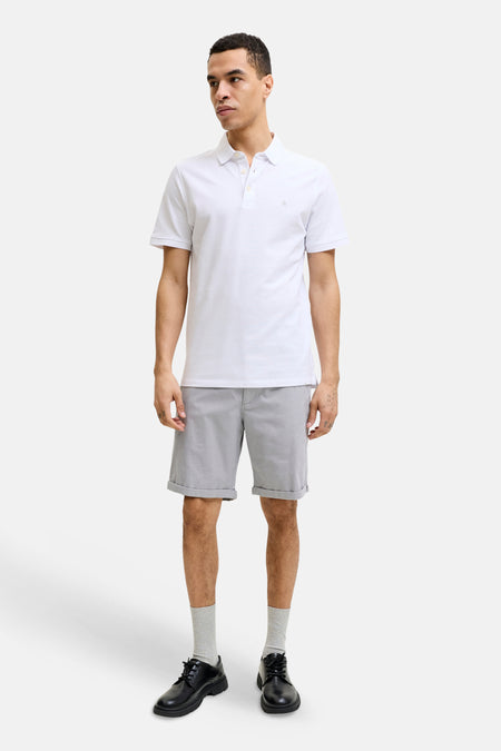 Short gris de JACK & JONES JEANS INTELLIGENCE avec motif subtilement tissé, une poche passepoilée avec un bouton marron foncé et un polo blanc.
