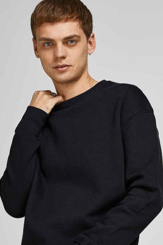Gilet noir de CORE BY JACK & JONES, avec col rond et manches longues, porté par un homme avec des bagues.