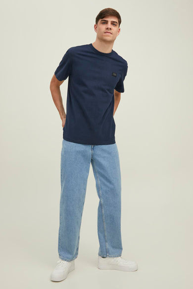 T-shirt à manches courtes bleu marine de CORE BY JACK & JONES avec une petite étiquette sur la poitrine, porté avec un jean bleu clair et des baskets blanches, vue de face.
