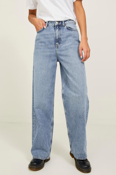 Jean large en denim bleu de JJXX, avec un lavage clair et combiné avec un t-shirt blanc et des chaussures noires.