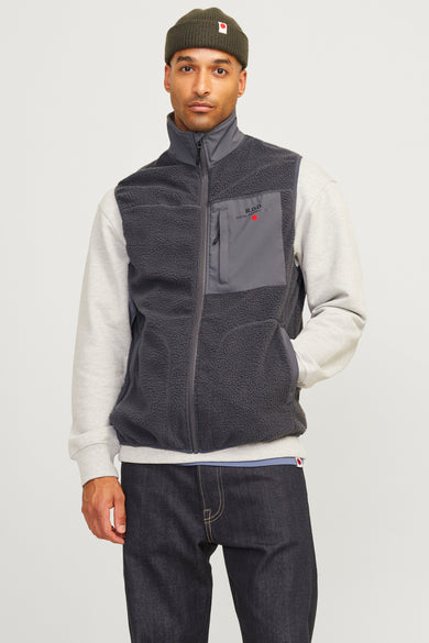 Gilet gris de Royal Denim Division, avec texture sherpa et un g gis pull, jeans foncés et baskets argentées.