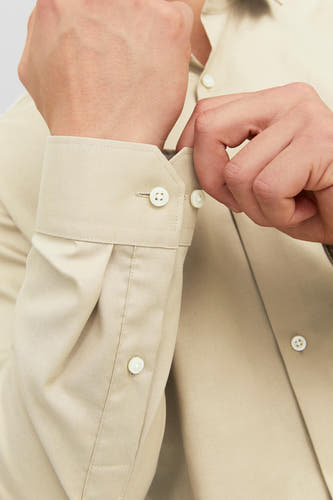 Chemise homme beige à longues manches de PREMIUM by JACK & JONES, gros plan d'un homme fermant le nœud de la poignée.