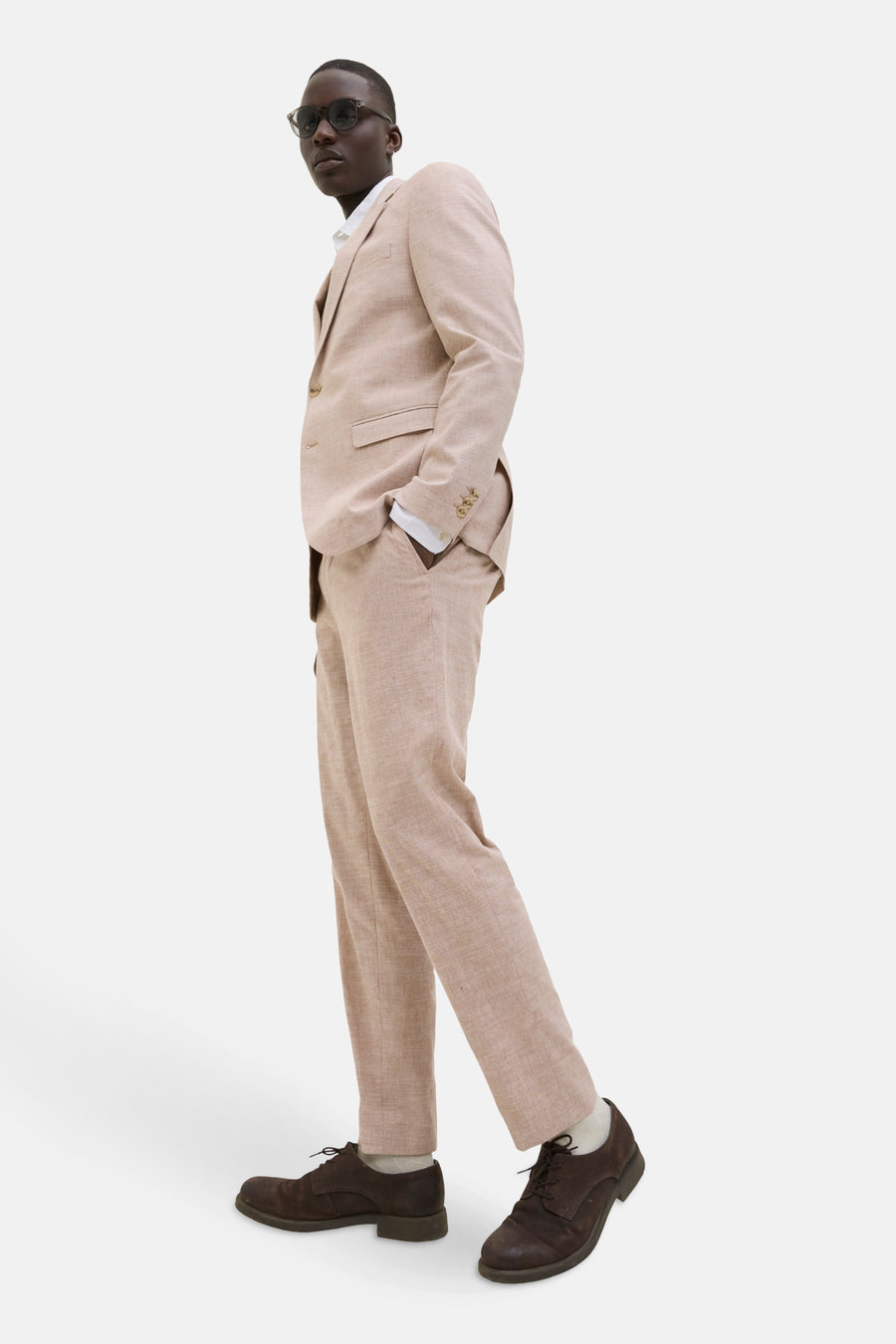 Man in beige pak met zonnebril en bruine schoenen.