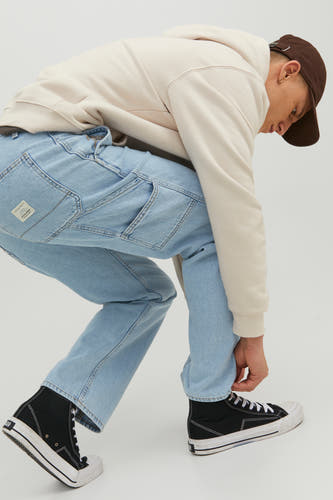 Jean en denim bleu clair large de JACK & JONES JEANS INTELLIGENCE, avec des poches et des plis légers, associé à une hoodie beige et des baskets noires.