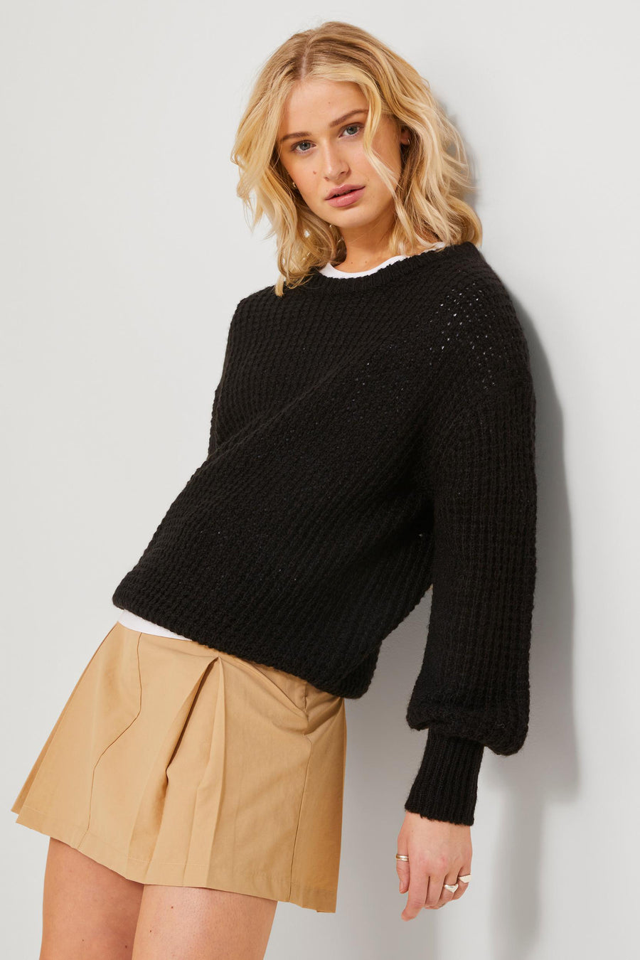 Jupe beige courte de JJXX, associée à une veste tricotée noire et un t-shirt blanc.
