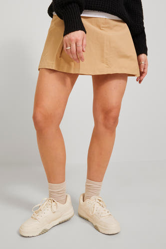 Jupe courte beige de JJXX, avec une silhouette en A, associée à des sneakers crème et des chaussettes.