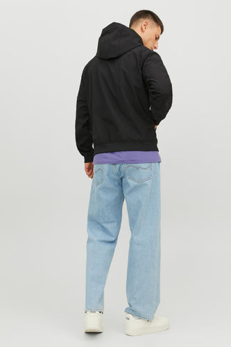 Achterkant van een man in zwarte hoodie, paars shirt, wijde jeans en witte sneakers.