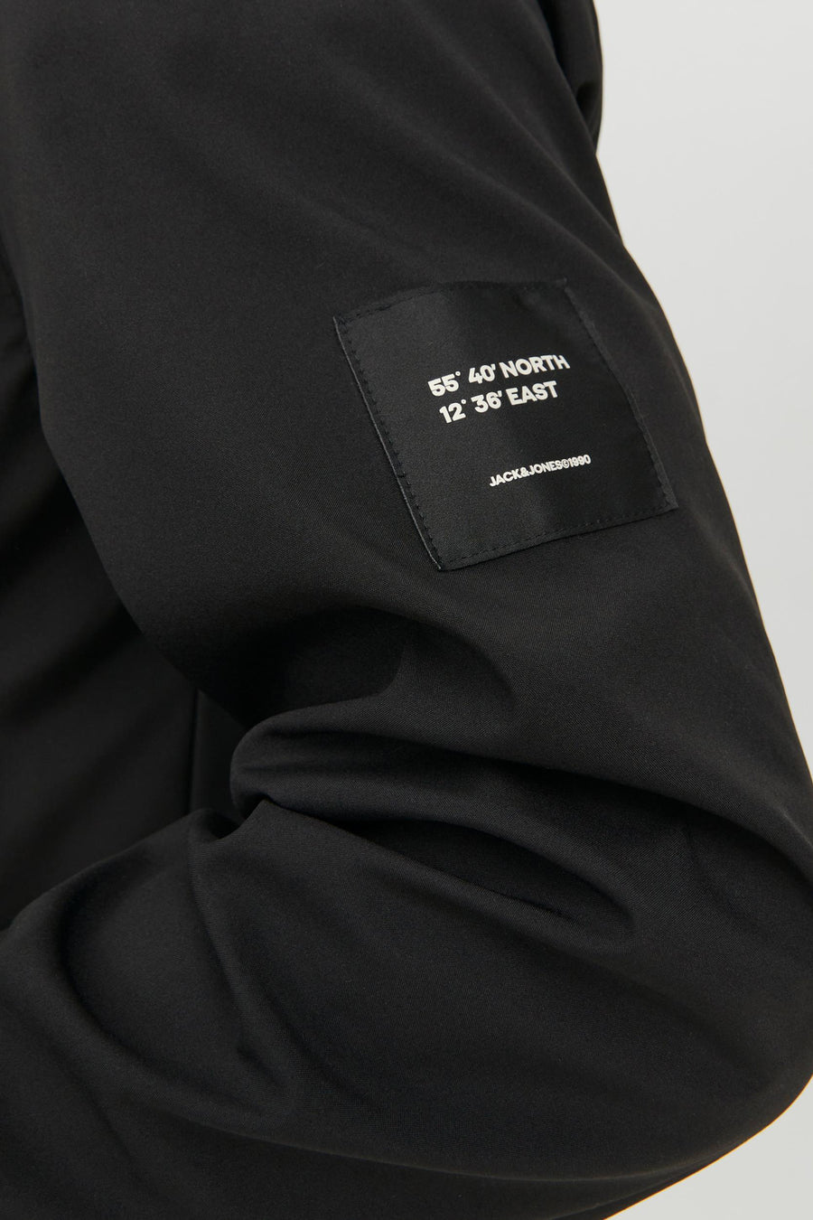 Close-up van een zwart kledingstuk met een label met coördinaten en "JACK&JONES©1990".