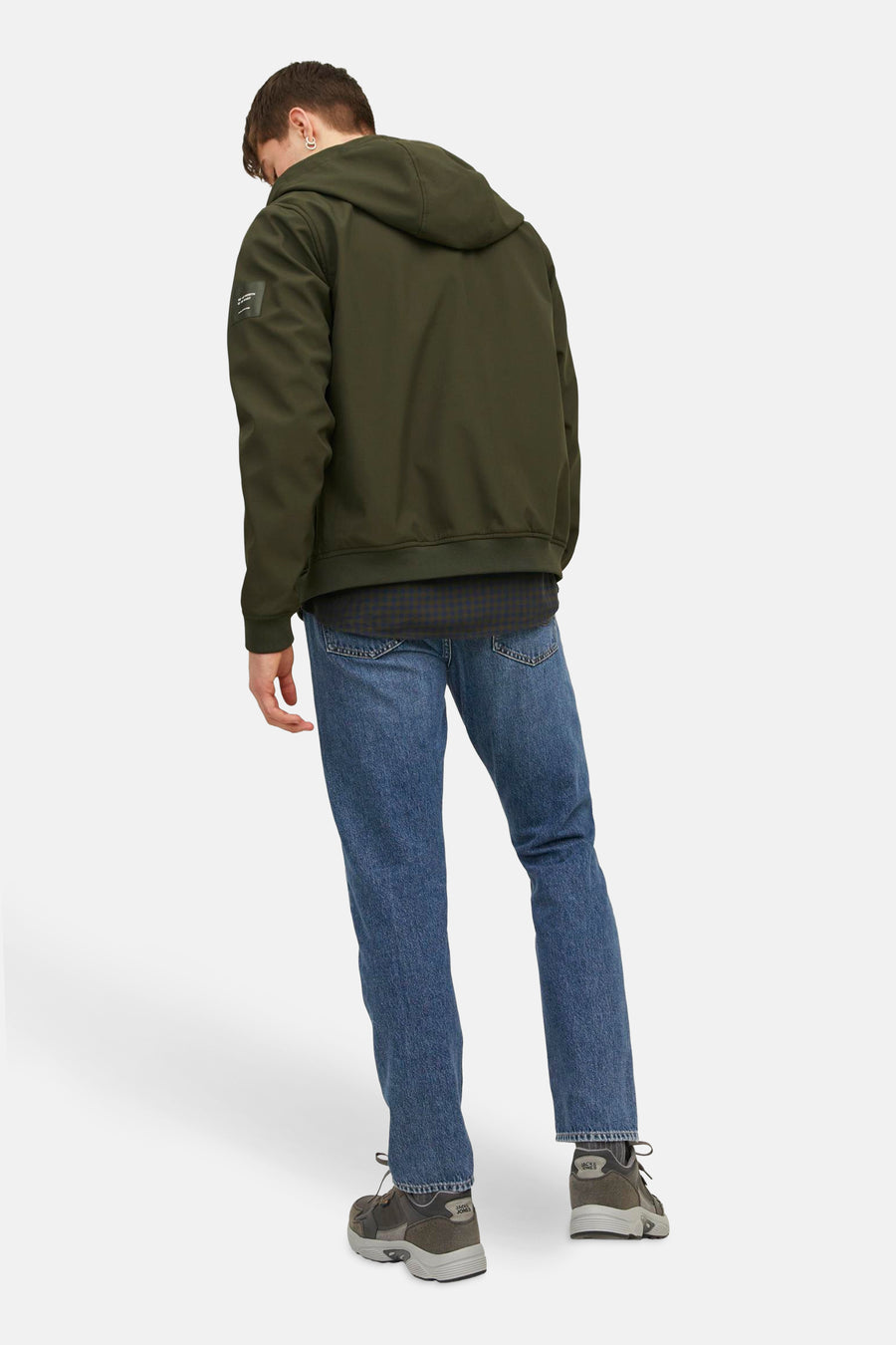 Achterkant van een man in groene jas, blauwe jeans en grijze sneakers.