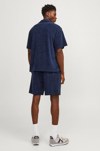 Blauw hemd met korte mouwen van PREMIUM by JACK & JONES, achterkant gezien, met bijpassende short en sneakers.
