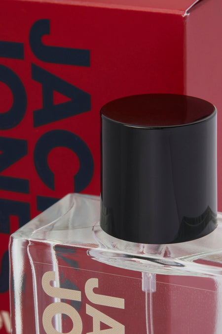 Parfum rouge d'ACCESSORIES BY JACK & JONES avec un bouchon noir et un emballage partiellement visible.