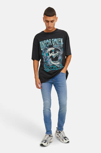 Jean skinny en denim bleu clair de JACK & JONES JEANS INTELLIGENCE, porté avec un T-shirt noir à imprimé graphique et des baskets blanches.