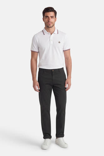 Pantalon chino noir de Jack & Jones Jeans Intelligence, avec jambes longues et ourlet retroussé, combiné avec un polo blanc et des baskets blanches.