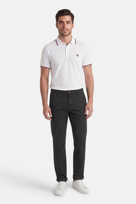 Pantalon chino noir de Jack & Jones Jeans Intelligence, avec jambes longues et ourlet retroussé, combiné avec un polo blanc et des baskets blanches.