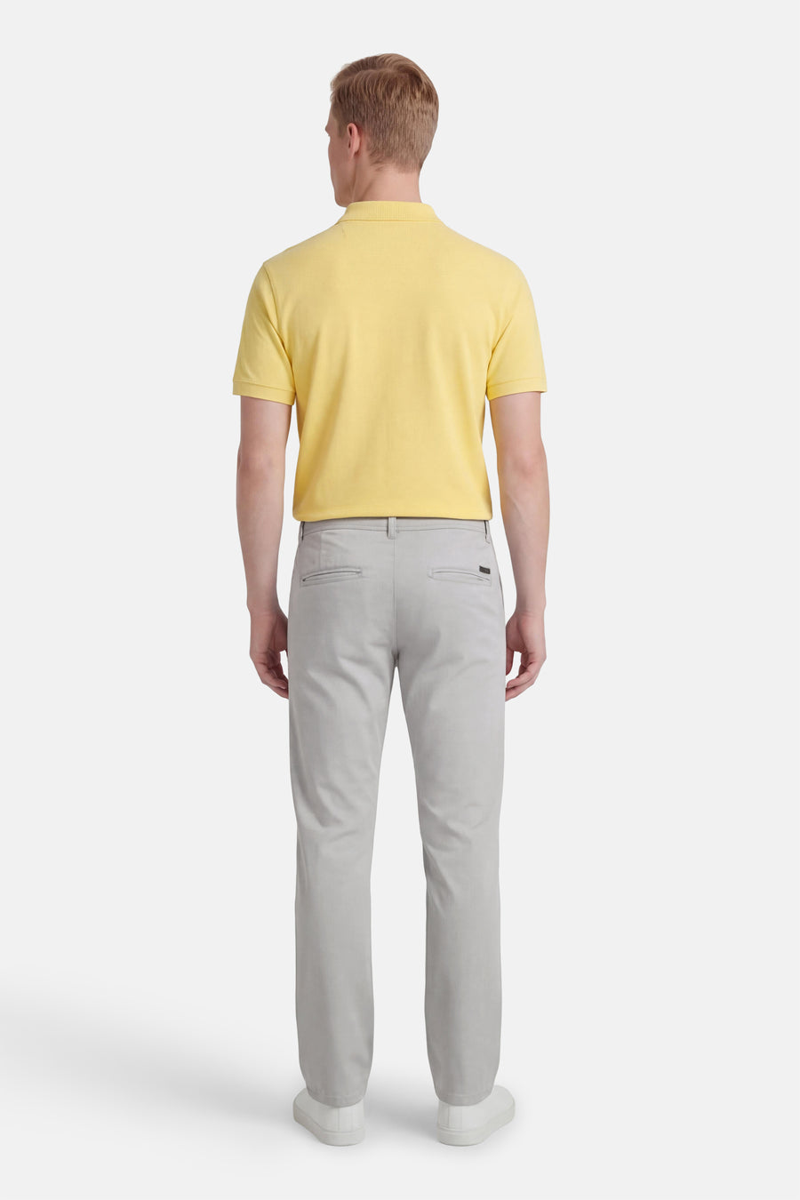 Pantalon chino gris de JACK & JONES JEANS INTELLIGENCE, vu de dos, combiné avec un polo jaune et des chaussures blanches.