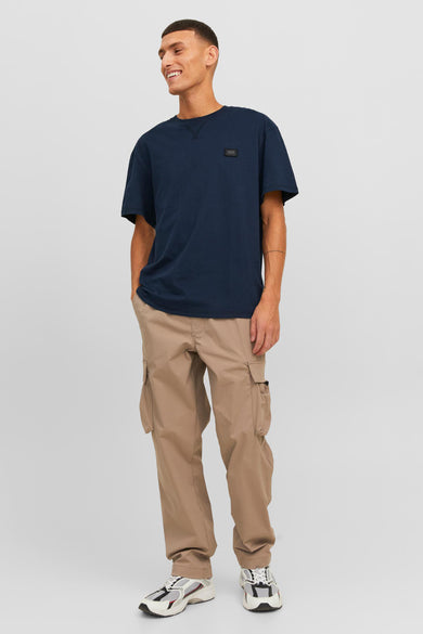 T-shirt à manches courtes bleu marine de CORE BY JACK & JONES avec petit logo sur la poitrine, porté dans une photo lifestyle avec un pantalon cargo beige et des baskets