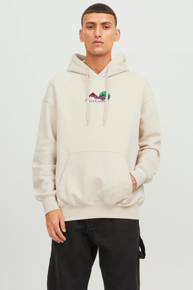 Man met beige hoodie met opdruk en zwarte broek.
