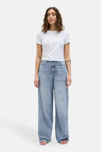 Jean bleu clair, large de JJXX, porté un un-shirt-shirt blanc et pieds nus.