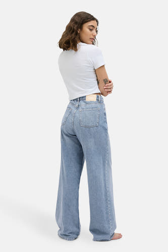 Jean bleu clair large de JJXX, avec des poches arrière et une étiquette de marque sur la ceinture, porté avec un T-shirt blanc.