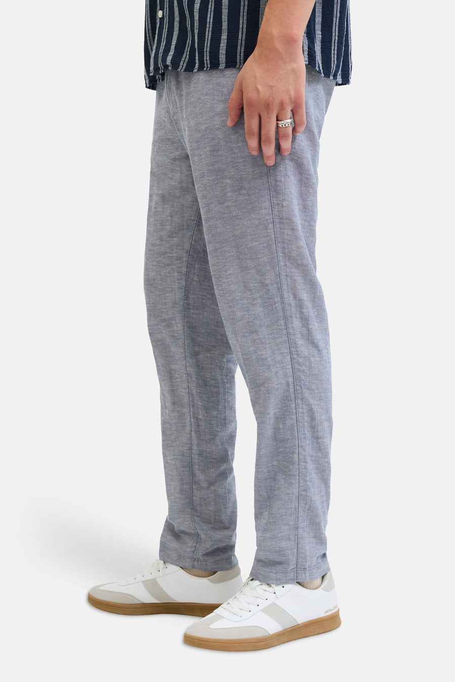 Chino bleu de JACK & JONES JEANS INTELLIGENCE, avec une texture légère, porté avec des baskets blanches et une chemise rayée.