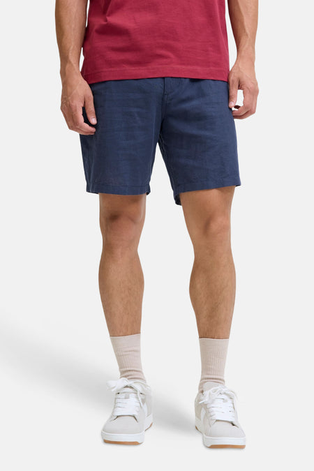 Short bleu de JACK & JONES JEANS INTELLIGENCE, porté par un homme avec un T-shirt rouge, des lunettes de soleil et des baskets blanches.