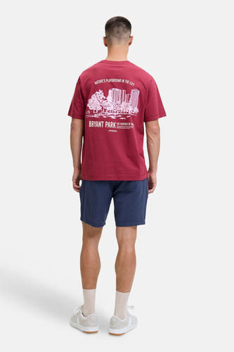 Short bleu de JACK & JONES JEANS INTELLIGENCE, porté par un homme avec un T-shirt bordeaux à imprimé blanc et des baskets beiges, vu de dos.