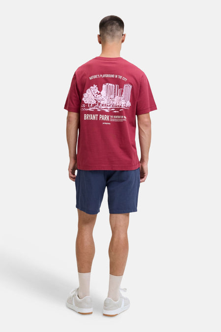 Short bleu de JACK & JONES JEANS INTELLIGENCE, porté par un homme avec un T-shirt bordeaux à imprimé blanc et des baskets beiges, vu de dos.