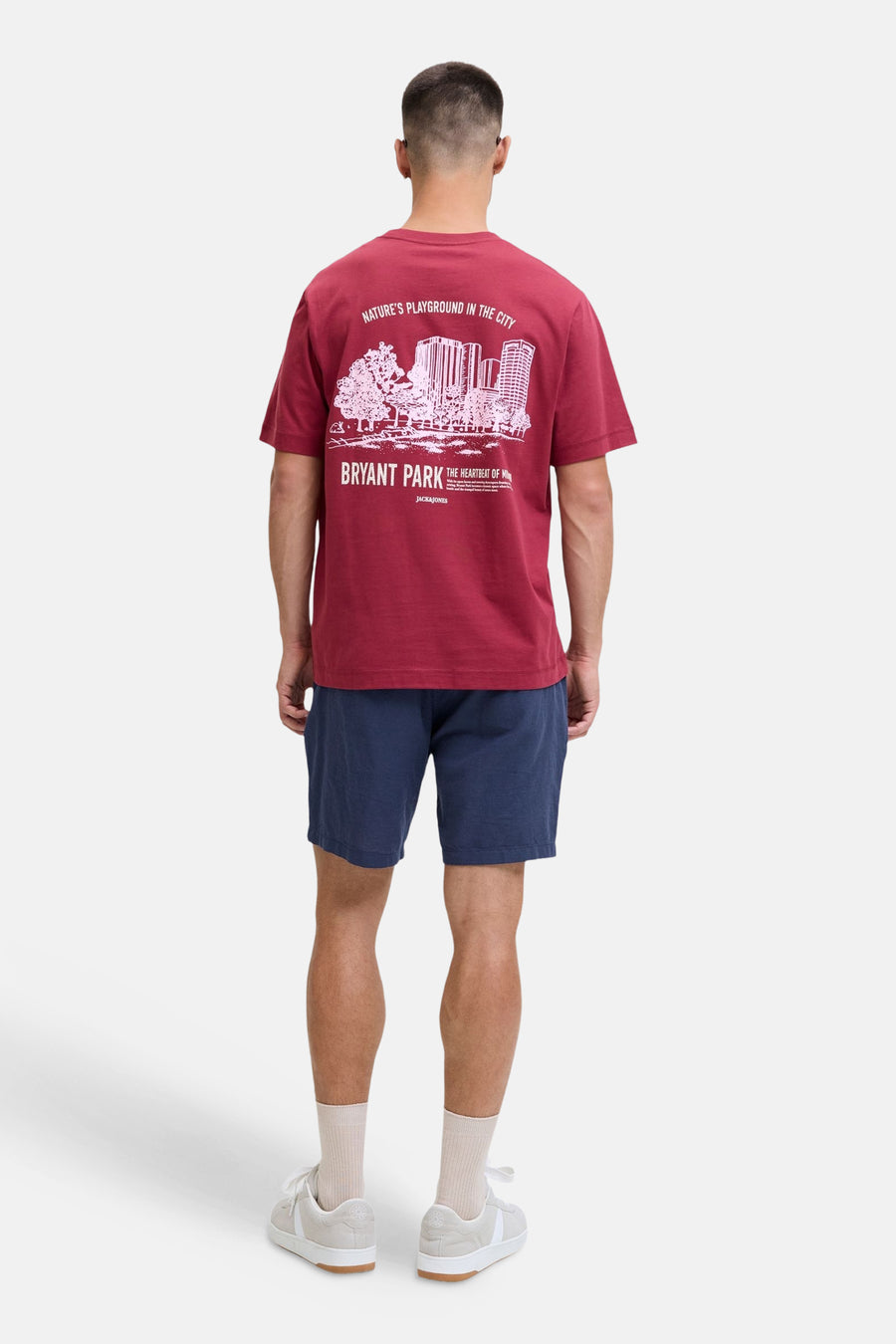 Short bleu de JACK & JONES JEANS INTELLIGENCE, porté par un homme avec un T-shirt bordeaux à imprimé blanc et des baskets beiges, vu de dos.