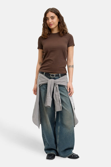 T-shirt marron à manches courtes de JJXX, avec des tatouages sur les bras, associé à des jeans larges et un chemisier rayé autour de la taille.