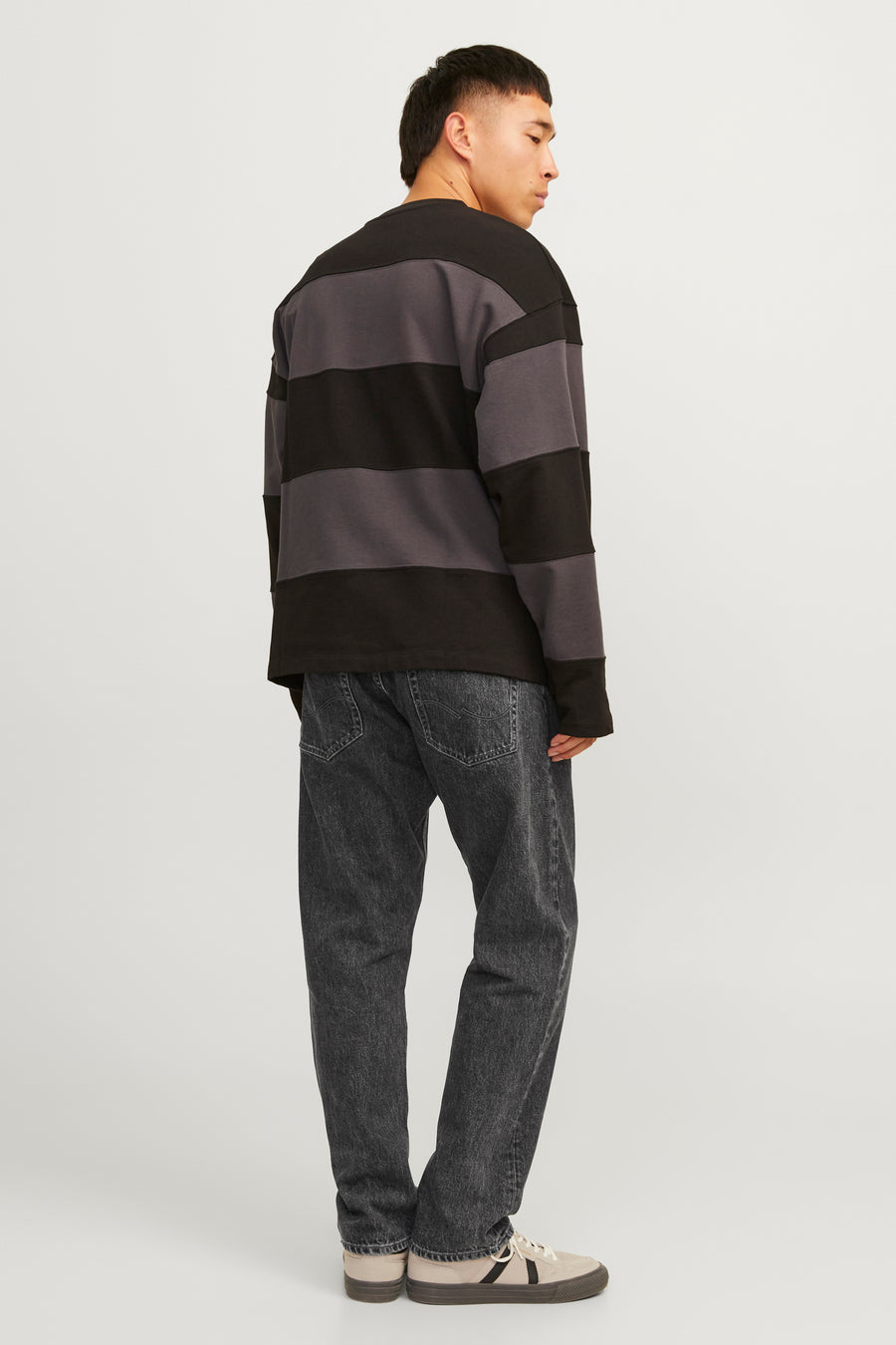Jean délavé noir de JACK & JONES JEANS INTELLIGENCE, porté avec un pull rayé et des baskets basses.
