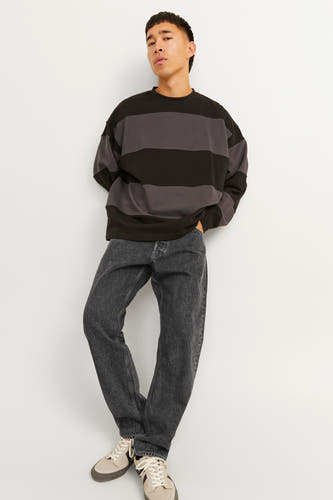 Jean en denim noir large de JACK & JONES JEANS INTELLIGENCE, porté avec un pull rayé et des baskets.