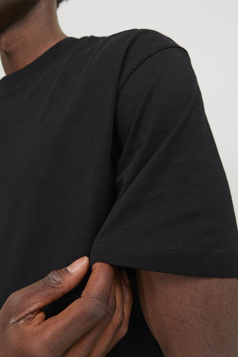 T-shirt noir à manches courtes de ORIGINALS BY JACK & JONES, avec une couture visible et une personne tirant sur la manche.