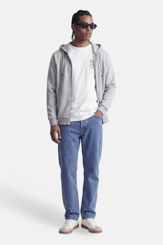Sweat à capuche zippé gris de CORE BY JACK & JONES, avec capuche et poche avant, porté sur un t-shirt blanc, jean bleu et baskets blanches, vue de face.