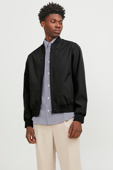 Manteau court noir de PREMIUM par JACK & JONES, porté avec un chemisier rayé et un pantalon beige.