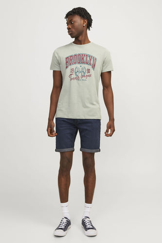 Donkerblauwe denim jeansshort van JACK & JONES JEANS INTELLIGENCE, met opgerolde pijpen en gedragen door een man met sneakers en sokken.
