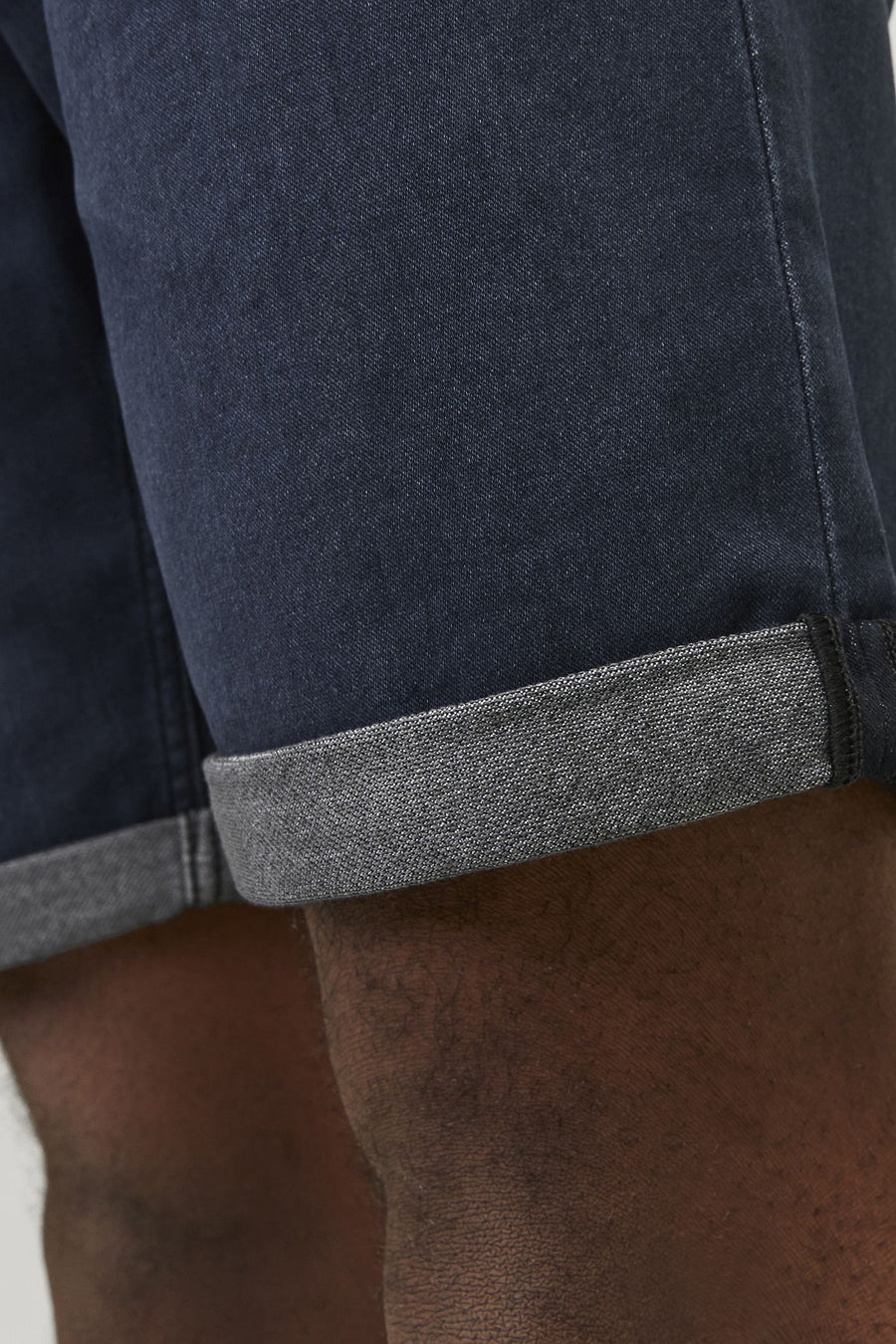 Donkerblauwe jeansshort van JACK & JONES JEANS INTELLIGENCE, met opgerolde zoom en detail van de been.