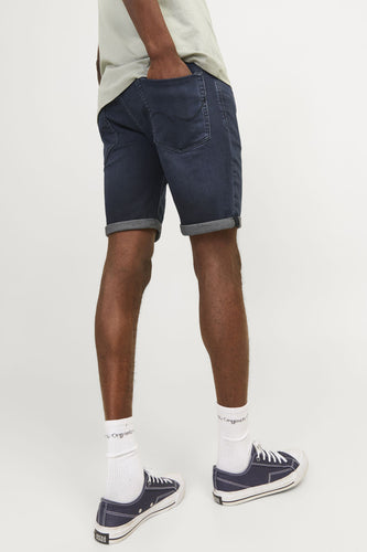 Donkerblauwe jeansshort van JACK & JONES JEANS INTELLIGENCE, met opgerolde pijpen en witte sokken met donkerblauwe schoenen.

