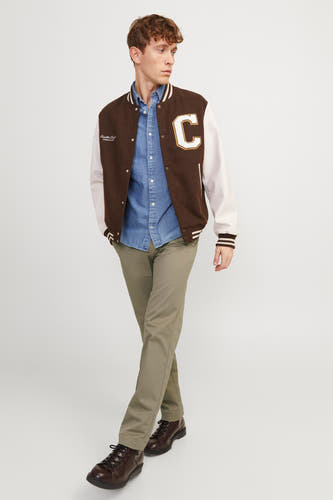 Chino beige de JACK & JONES JEANS INTELLIGENCE, porté par un homme avec une chemise en jean, un blouson universitaire marron et blanc avec la lettre 'C' et des chaussures richelieu marron foncé.